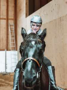 Kuvassa peruukkipäinen tyttö istuu hevosen selässä