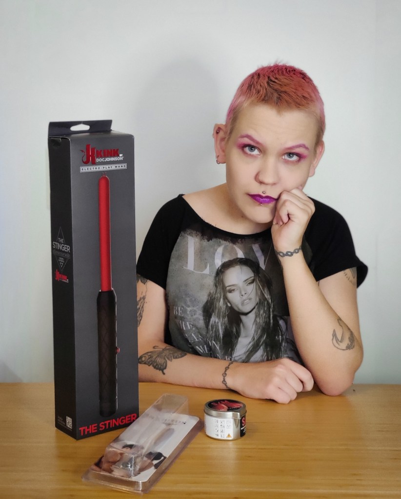 Pinja istuu pöydän ääressä, edelleen sähkökeppi, piikkipyörä ja bdsm-käyttöön tarkoitettu kynttilä.