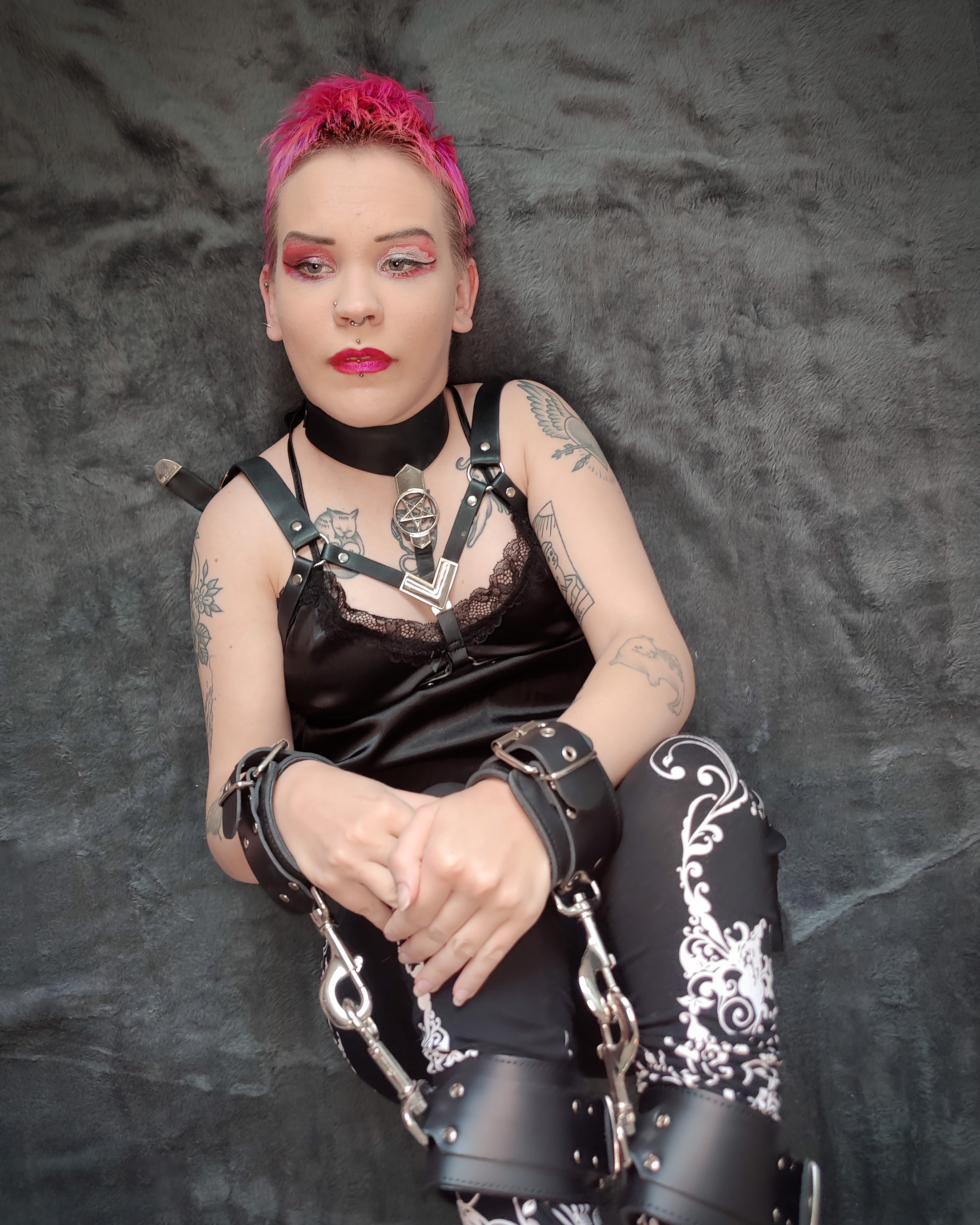 Kuvassa makaan selälläni polvet koukussa harmaalla taustalla. Ranteissa ja nilkoissa minulla on nahkaiset kahleet, jotka on yhdistetty toisiinsa niin, että käteni ovat kiinni jaloissani.