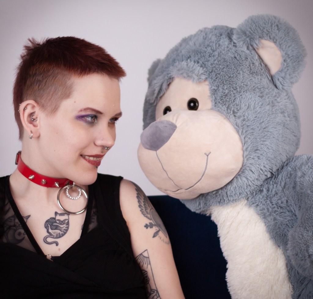 Lähikuva Pinjasta hymyilemässä hänen vasemmalla puolellaan olevalle suurelle pehmokarhulle. 