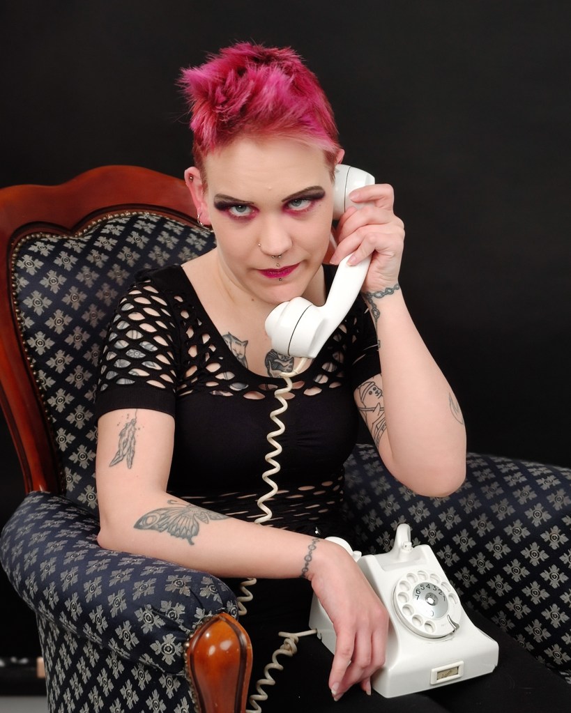 Pinja istuu koristeellisessa nojatuolissa ja katsoo kameraan tiukka ilme kasvoillaan. Hänen sylissään on vanha valkoinen puhelin, jonka luuria hän pitää korvallaan kuin kuuntelisi sitä. Hänellä on mustat vaatteet, tukka ja meikki ovat pinkkejä.