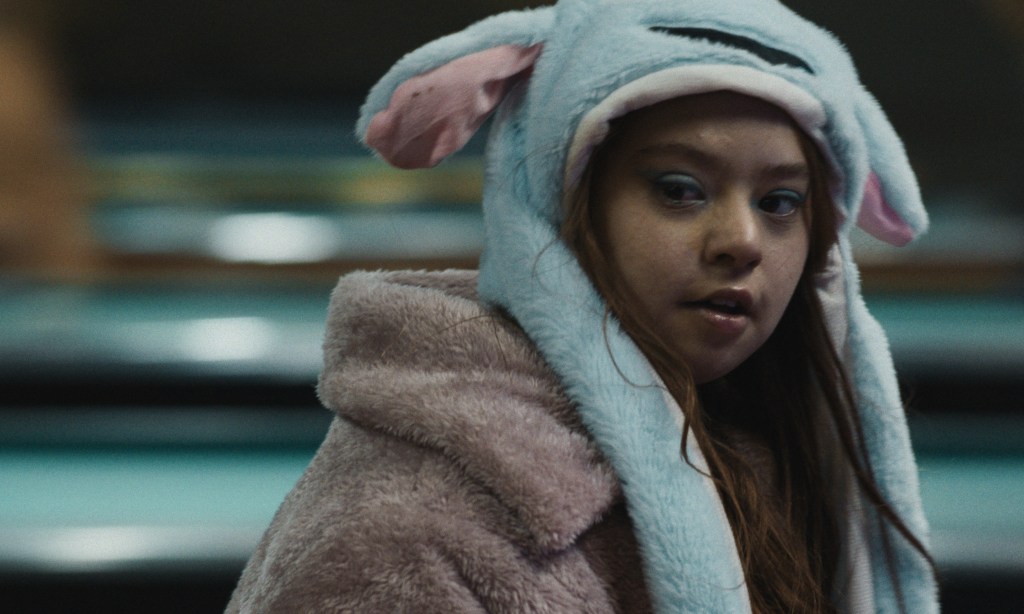 Nuori nainen, Colo (Kiara Supini), katsoo kameran suuntaan pörröinen hattu päässään.