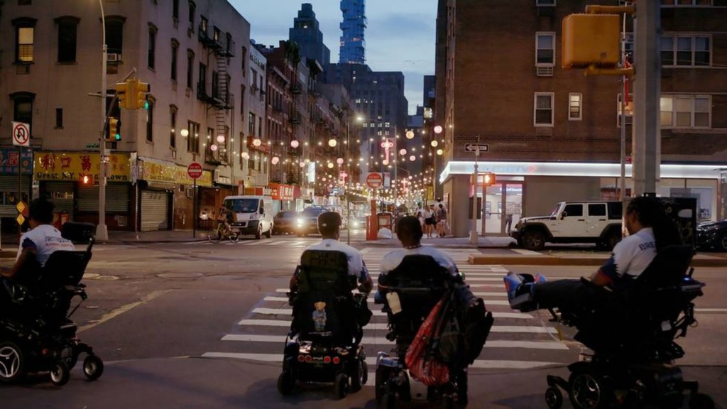 Elokuvan päähenkilöt navigoivat sähköpyörätuoleilla New Yorkissa.