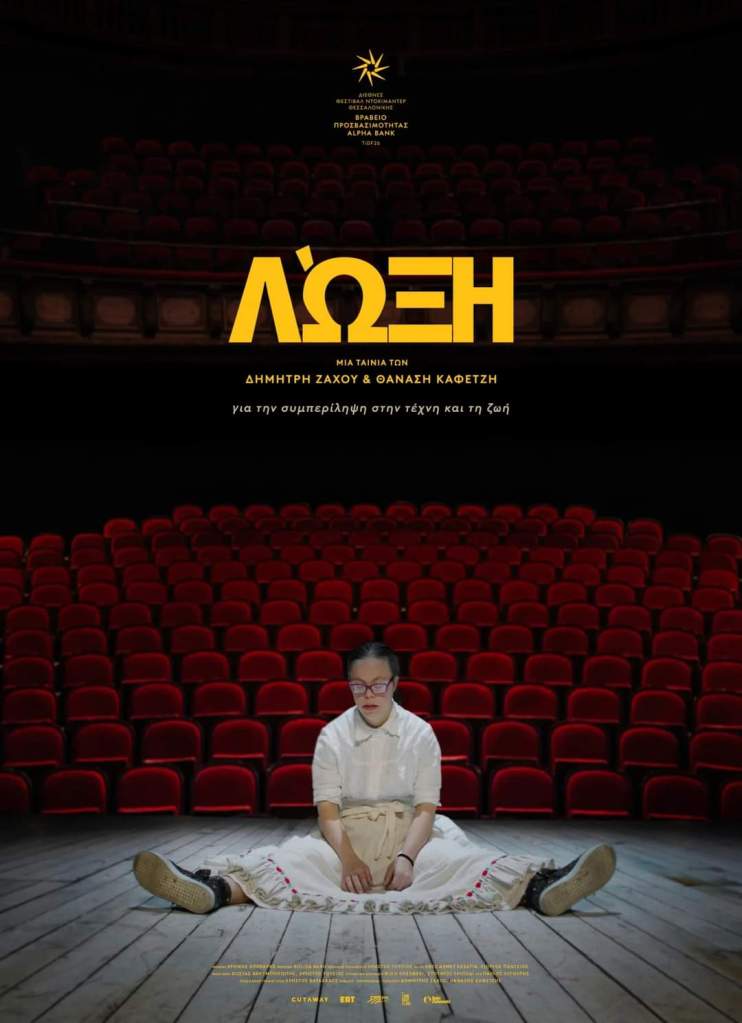 Loxy -elokuvan kreikankielinen juliste, jossa päähenkilö Loxy istuu teatterin lavalla, taustallaan joukko tyhjiä istuimia.