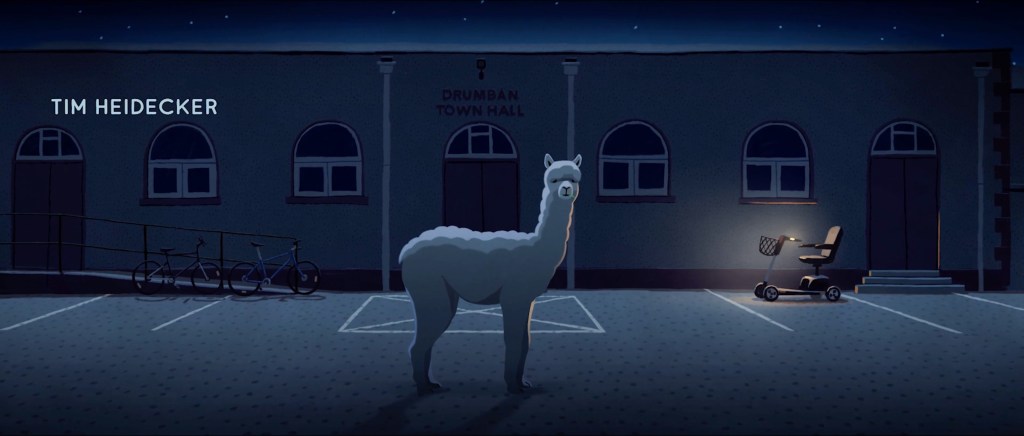 Alkutunnarista otetussa kuvakaappauksessa alpakka katselee hämmentyneenä kameraan Drumbanin kaupungintalon edessä. 