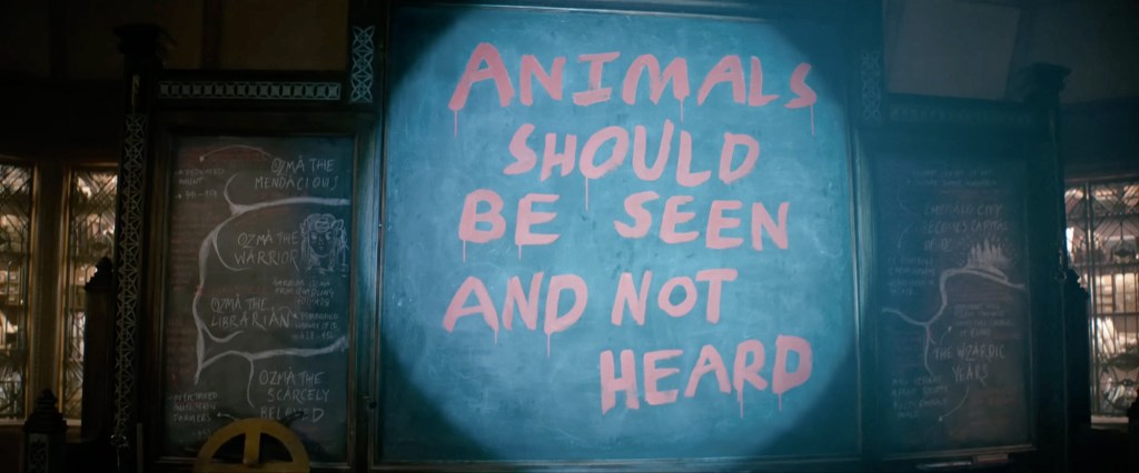 Professori Dillamondin luokkahuoneen taululle on kirjoitettu "Eläinten kuuluu näkyä, ei kuulua" kohtauksessa elokuvasta Wicked.